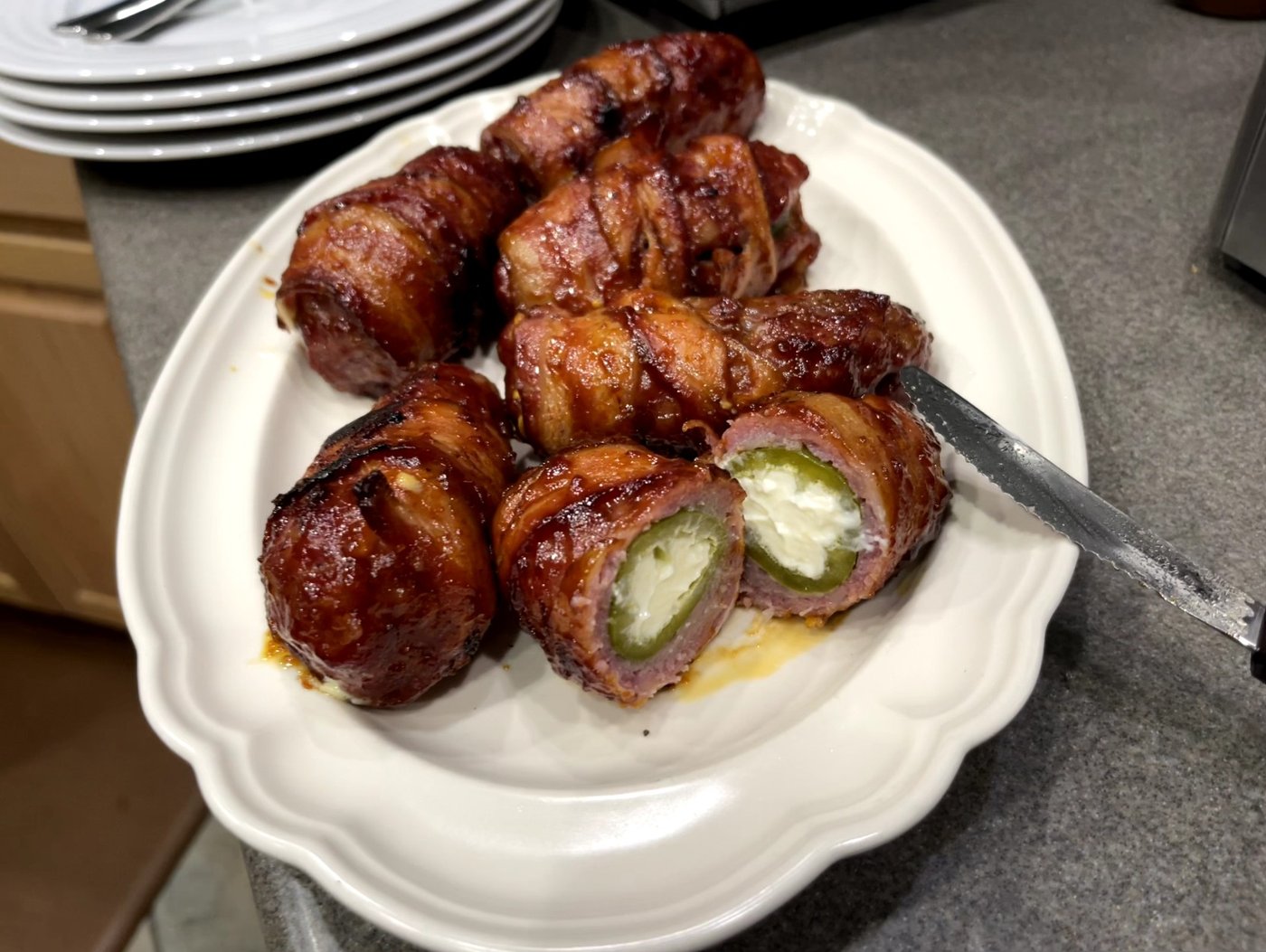 Bacon-wrapped smoked armadillo eggs on a plate, one cut open showing the cream cheese and jalapeño