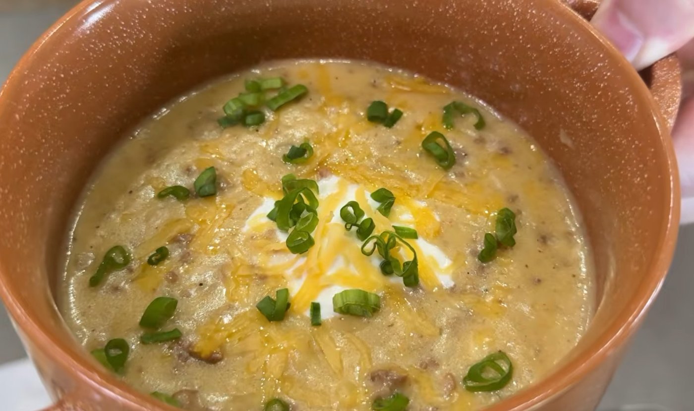 Bowl of spicy cheesy hamburger potato soup with sour cream, cheddar and green onions