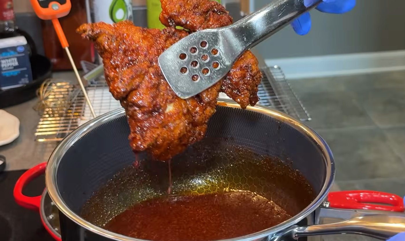 Fried chicken being lifted out of Nashville hot oil with tongs